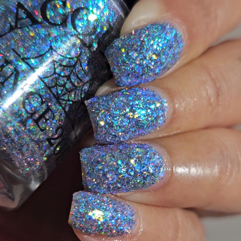 Close-up of a hand with nails painted in a dense holographic glitter nail polish, with the matching bottle partially visible in the background.