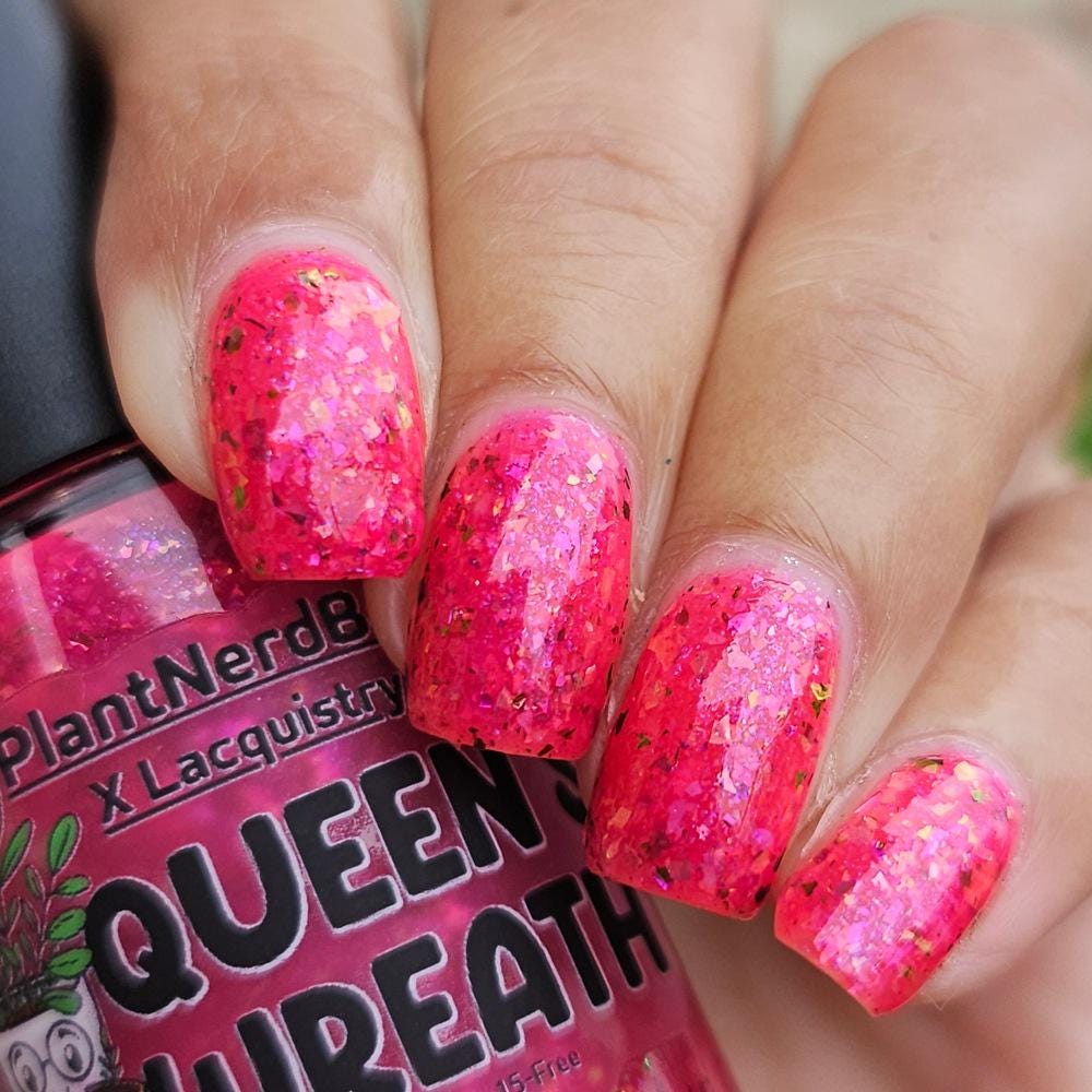 closeup of hand with medium skin and medium square nails with neon pink flake polish holding a nail polish bottle of the same color that says Queen Wreath PlantNerdBroom x Lacquistry