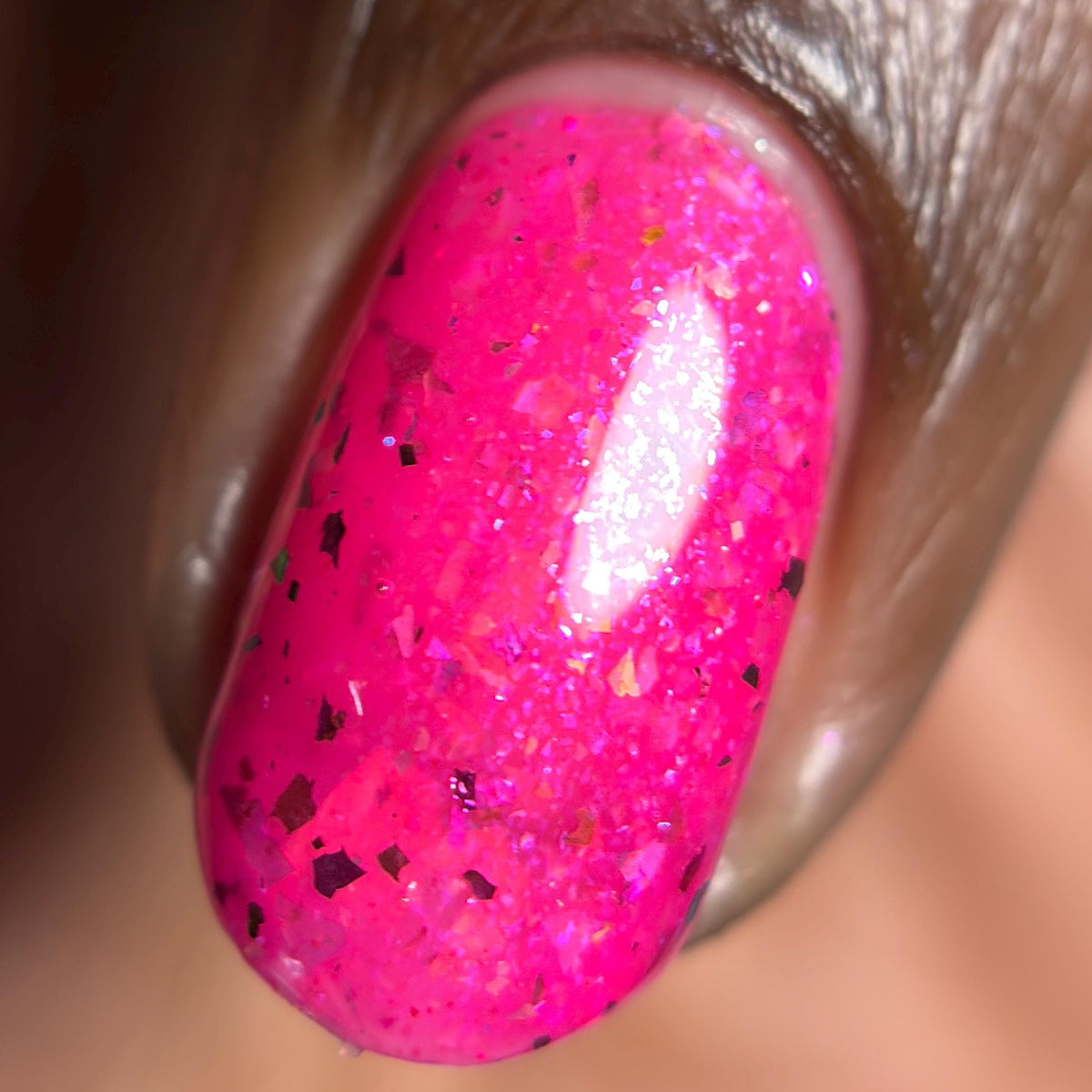 macro closeup of finger with dark skin and short nail with shiny neon pink flake nail polish 