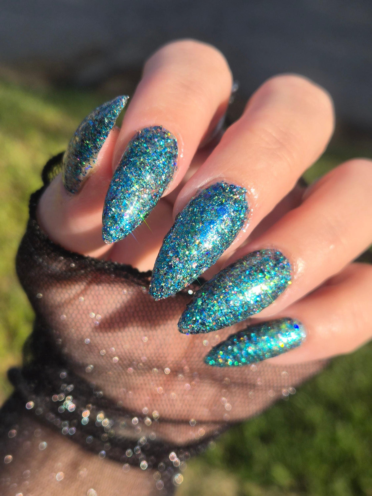 A close-up of a hand showcasing glittery teal blue nail polish