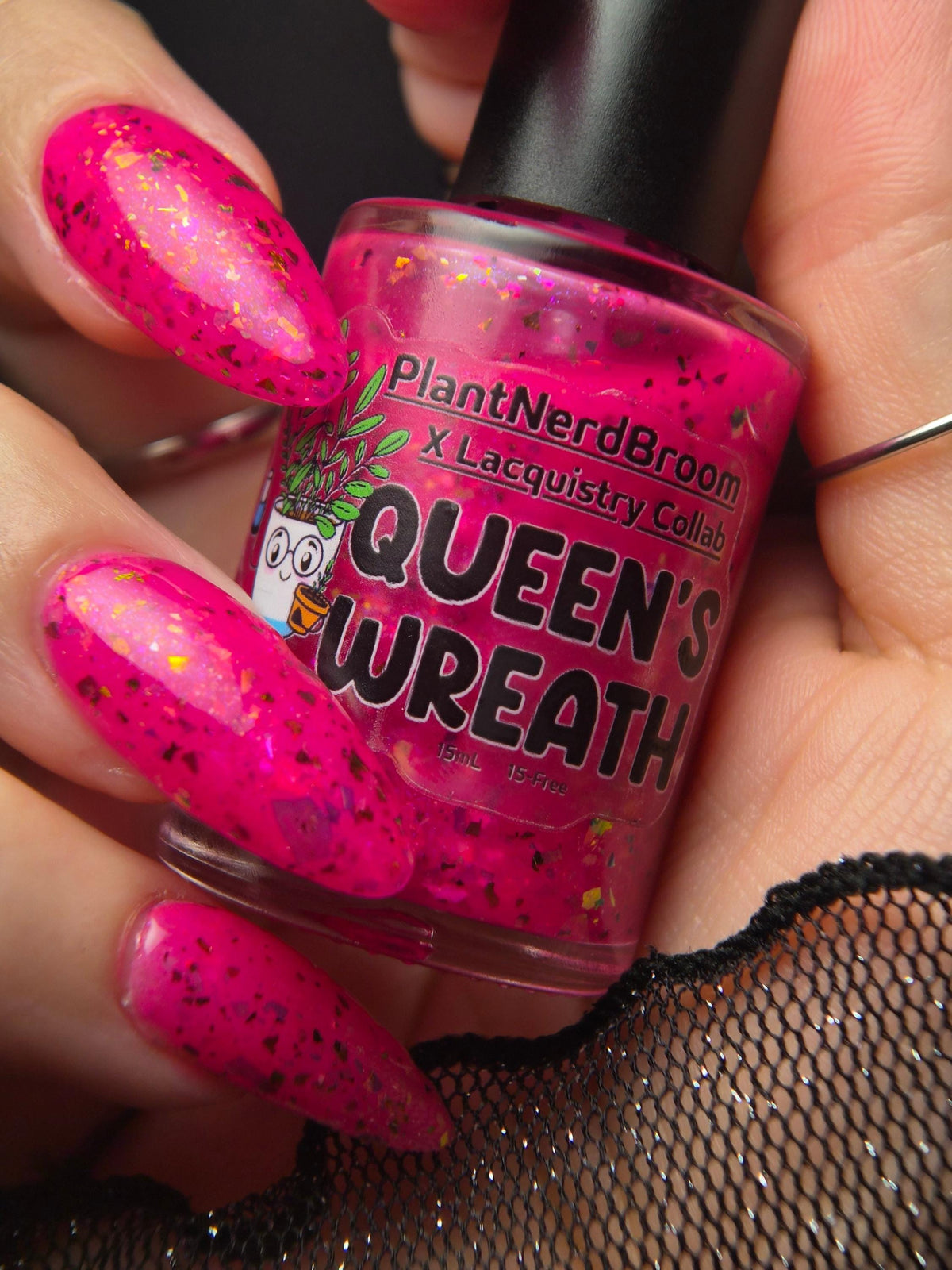 closeup of hand with light skin and long pointed nails with neon pink flake polish holding a nail polish bottle of the same color that says Queen Wreath PlantNerdBroom x Lacquistry