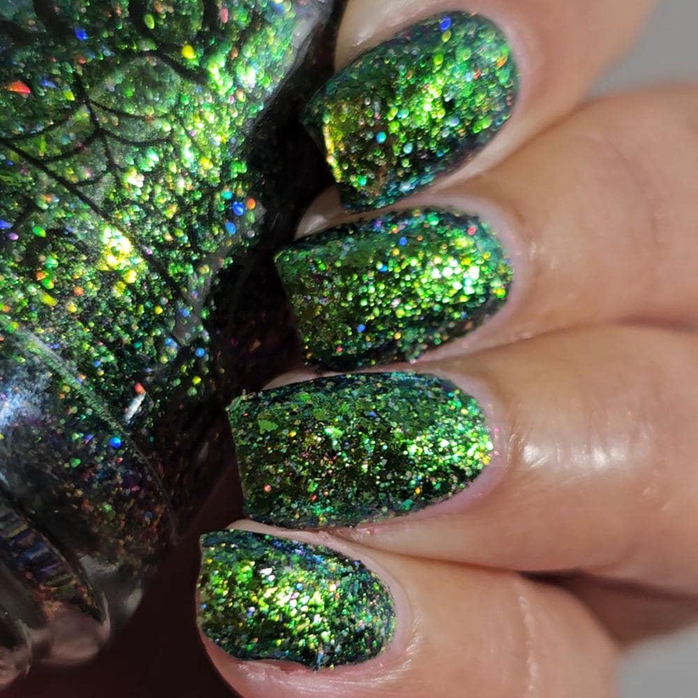 Close-up of a hand with manicured nails painted in a sparkling green glitter nail polish, with the matching bottle shown on the left.