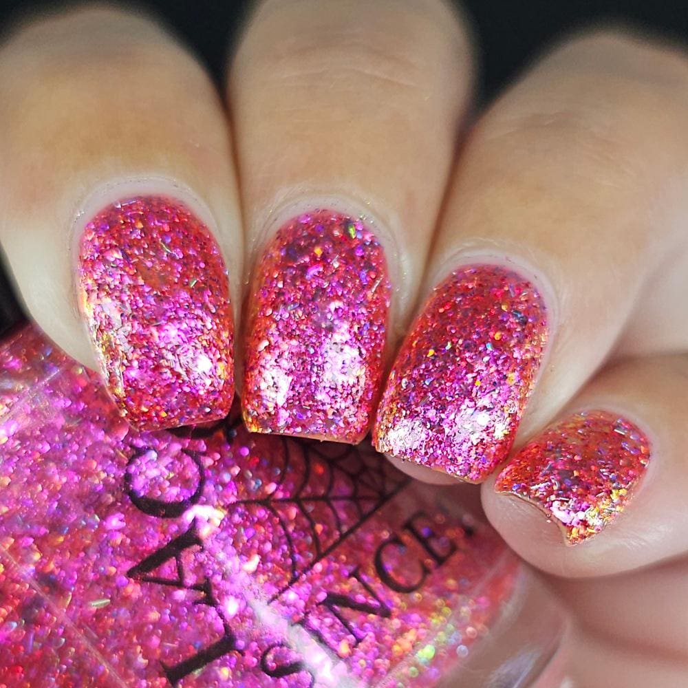 A close-up of a hand with manicured nails painted in a sparkling hot pink glitter nail polish, with the matching pink glitter bottle visible in the foreground. 