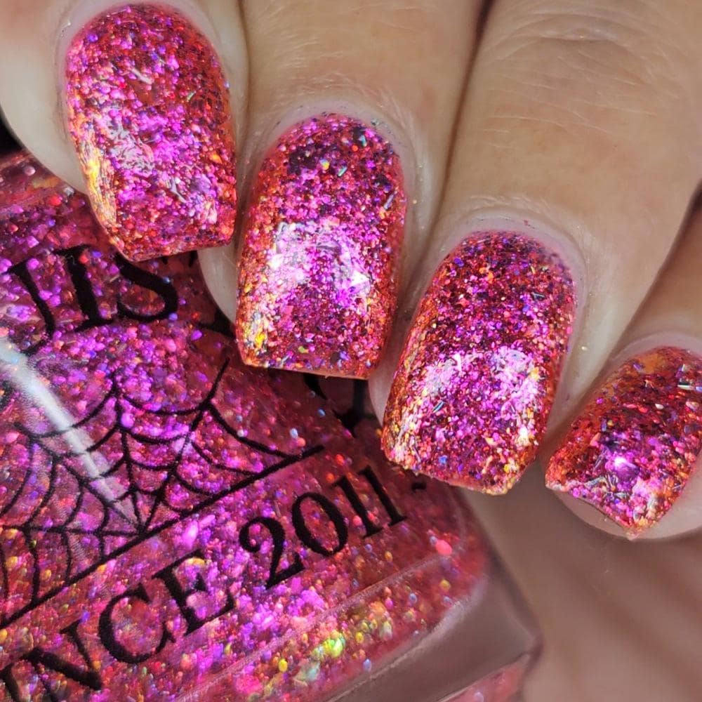 medium length square nails on medium skin tone wearing bright pink sparkling flake and glitter nail polish holding a bottle with a spiderweb of the same polish
