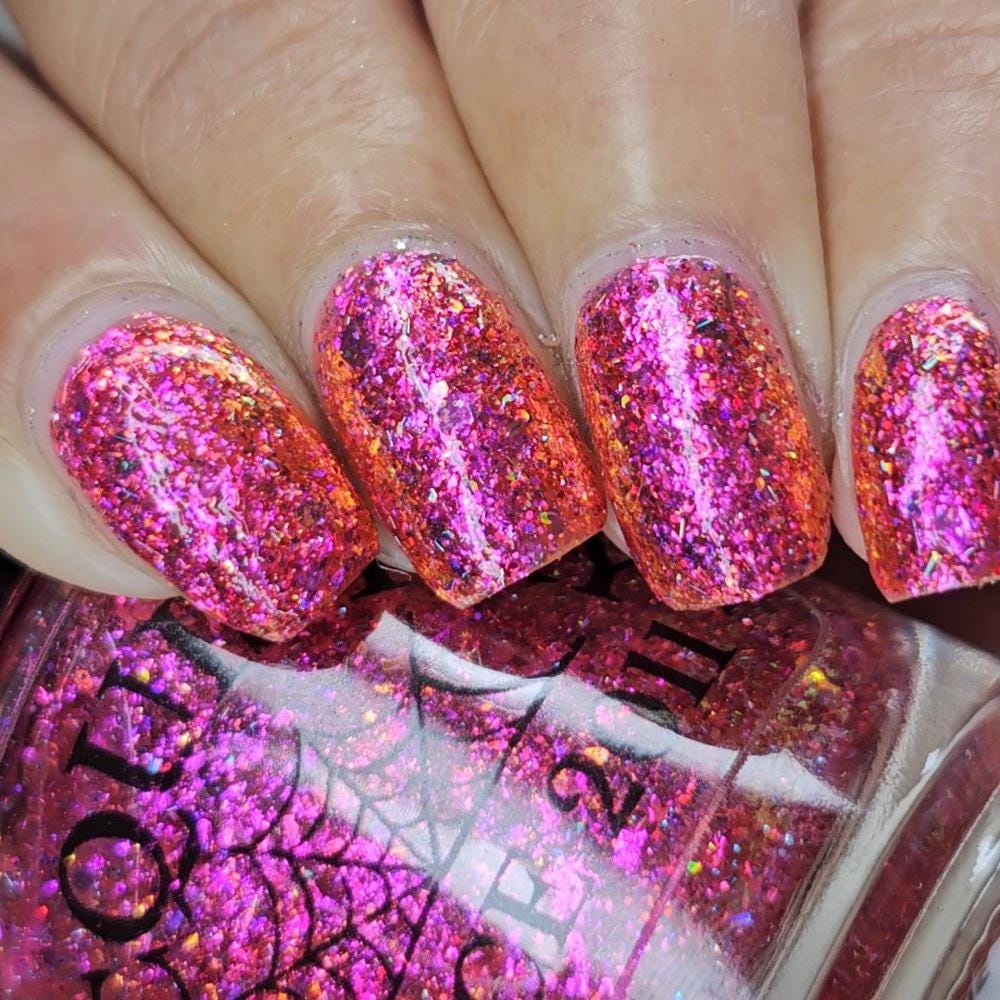 medium length square nails on medium skin tone wearing bright pink sparkling flake and glitter nail polish holding a bottle with a spiderweb of the same polish