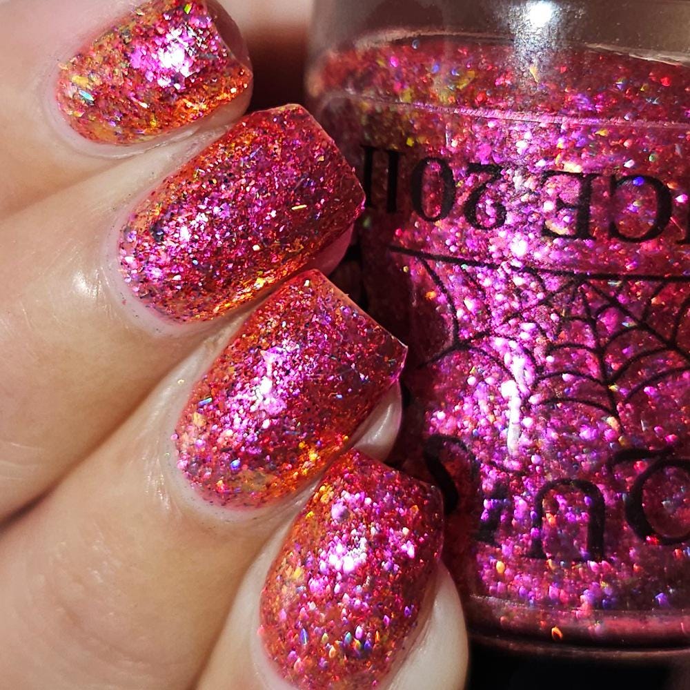 medium length square nails on medium skin tone wearing bright pink sparkling flake and glitter nail polish holding a bottle with a spiderweb of the same polish upside down
