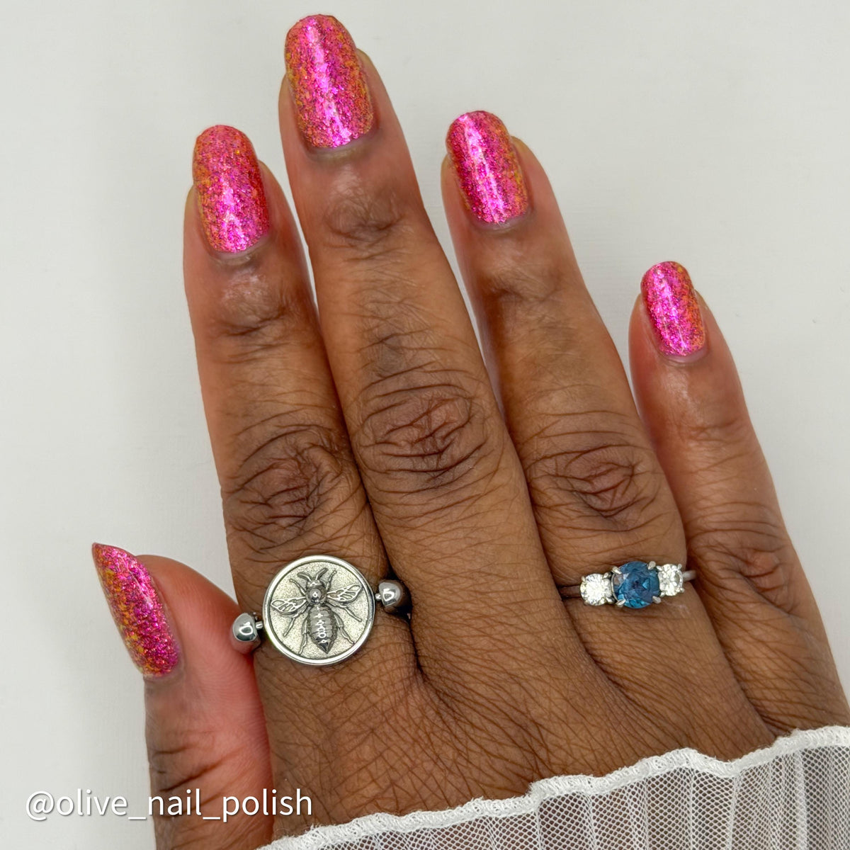 short nails on dark skin tone wearing bright pink sparkling flake and glitter nail polish with 2 silver rings