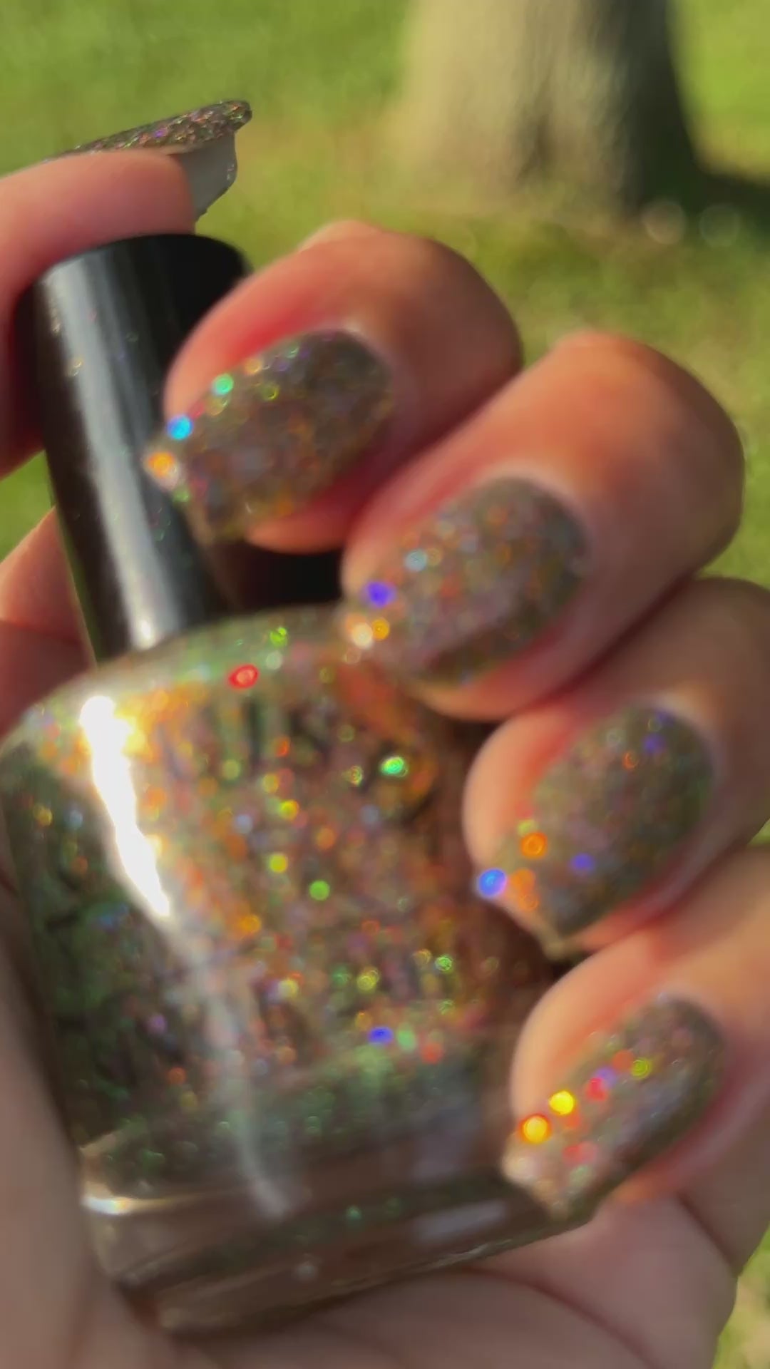video of nails painted with sparkly glittery polish showing pink, red, green, gold and orange glitters in a darkened base color with green reflective glitter moving in the sunlight