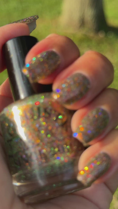 video of nails painted with sparkly glittery polish showing pink, red, green, gold and orange glitters in a darkened base color with green reflective glitter moving in the sunlight