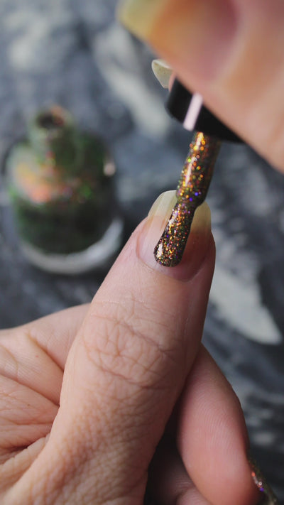 video of nails being painted with sparkly glittery polish showing pink, red, green, gold and orange glitters in a darkened base color with green reflective glitter